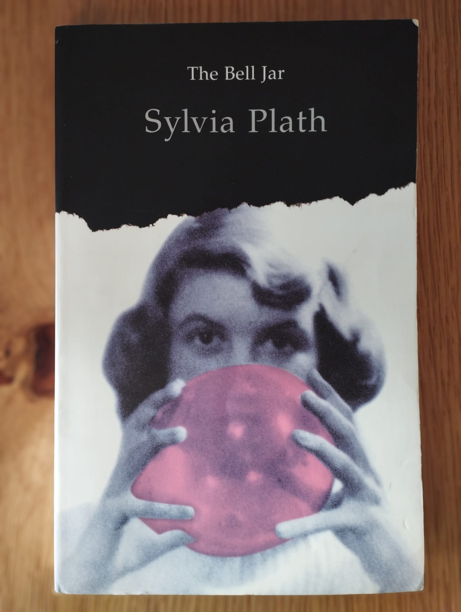 Book cover of The Bell Jar by Sylvia Plath, featuring a grayscale photo of a woman holding a pink disc, symbolizing the novel’s themes of mental health and identity.